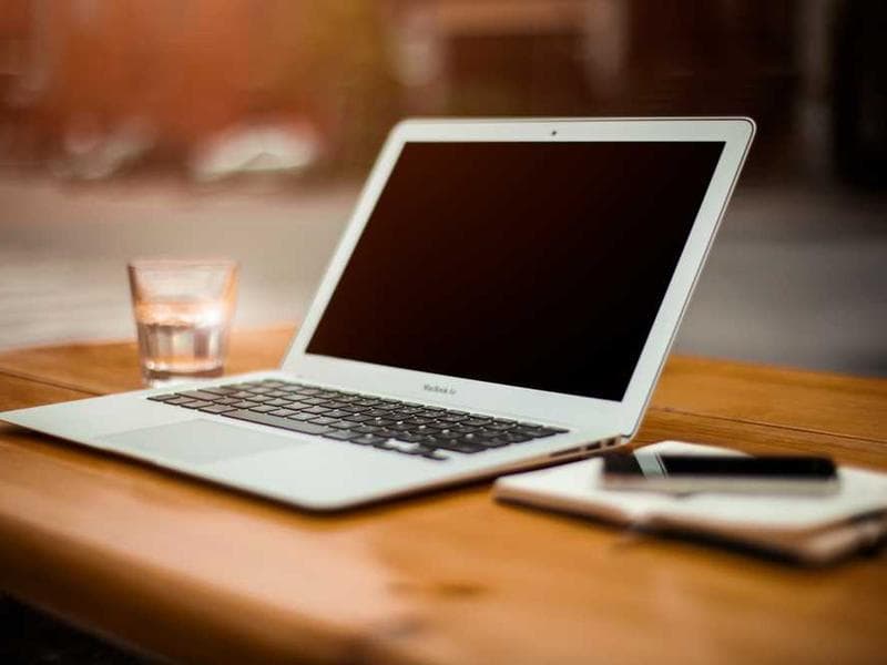 MacBook Air on wooden table with glass of water and notebook, warm lighting