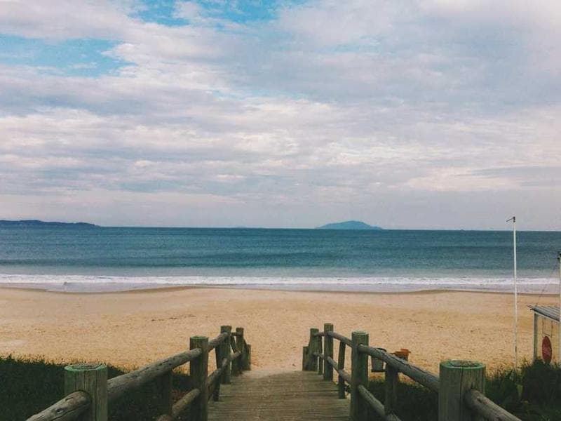 Wooden boardwalk leading to beach with ocean and distant islands under cloudy sky