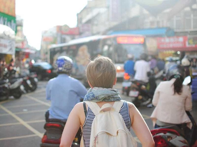 Person with white backpack walking through busy Asian street with parked motorcycles